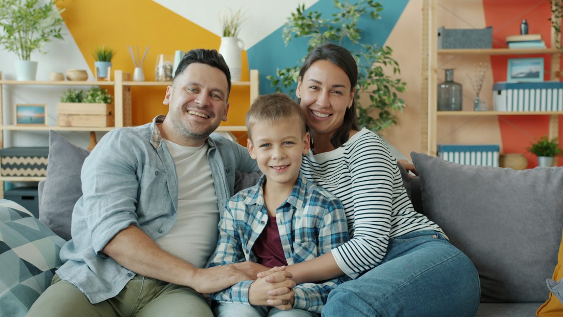 A smiling family of three sitting together on a sofa